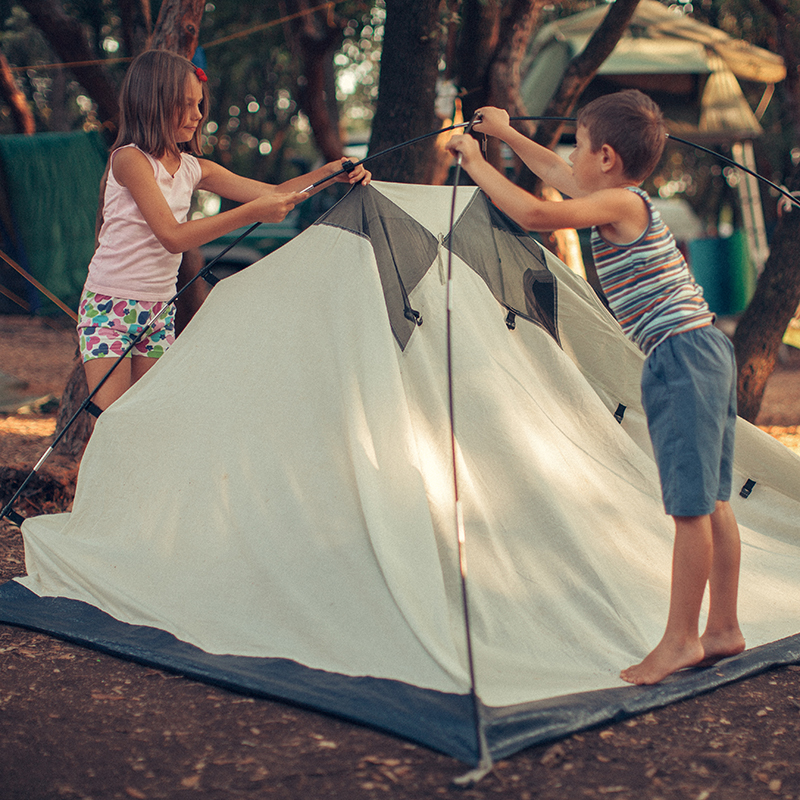 Little boy and girl preparing and setting up tent for camping.