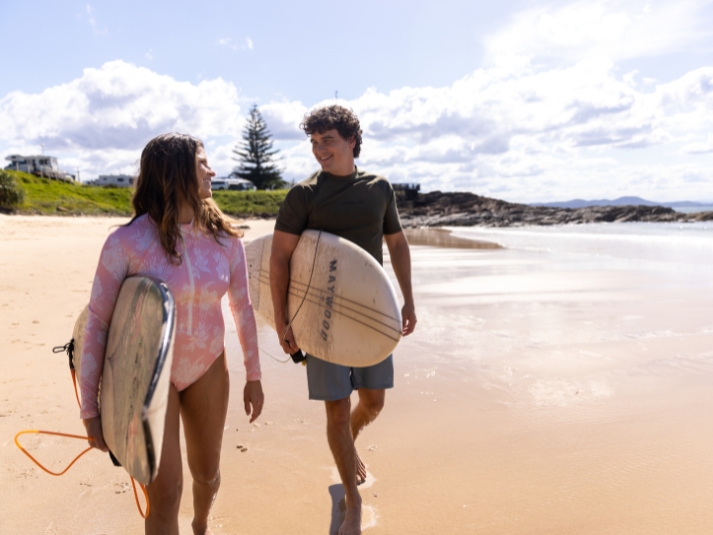 A male and female surfer walking along the beach with boards under arm.